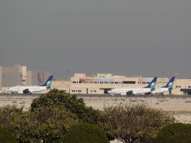 Three white Saudi Aramco Boeing 737-700 jets parked on the apron at King Fahd International Airport, with desert scrub in the foreground and terminal buildings behind