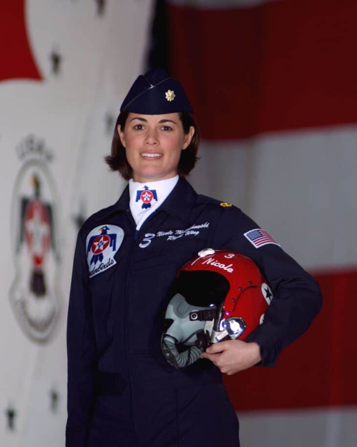 Maj. Nicole Malachowski in a dark blue Thunderbirds flight suit, holding a red, white and blue flight helmet