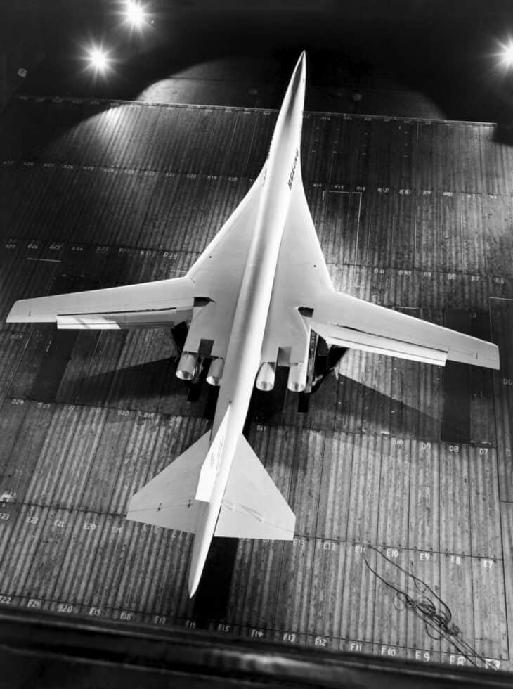 Overhead view of a large white Boeing swing-wing supersonic transport model with its wings unswept, mounted in the NASA Ames 40 by 80 foot wind tunnel
