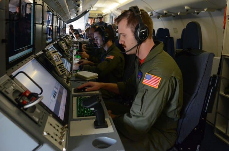 US Navy sailors wearing headsets working at the tactical mission consoles along the cabin of a P-8A Poseidon