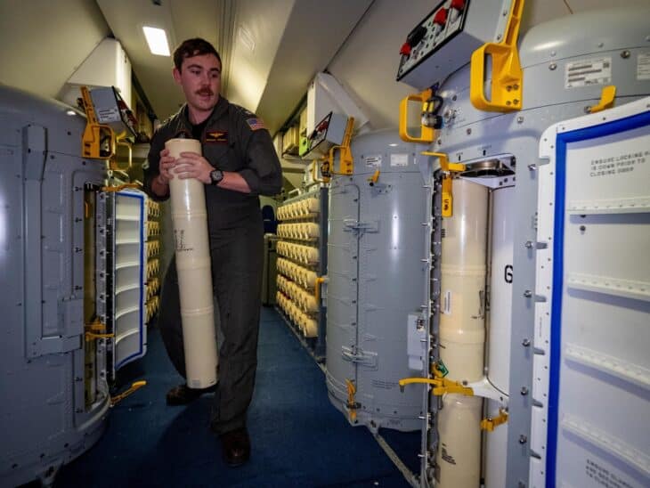 US Navy officer carrying a sonobuoy canister between the sonobuoy storage racks inside a P-8A Poseidon cabin