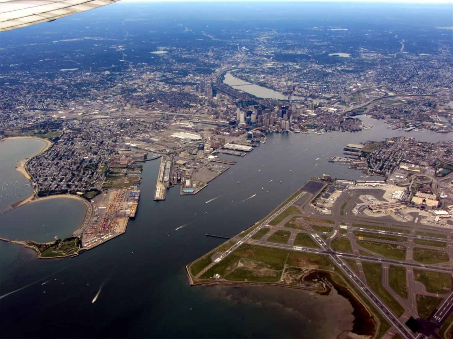 Aerial view of Boston Logan International Airport's runways on the edge of Boston Harbor, with the shipping channel and downtown Boston beyond