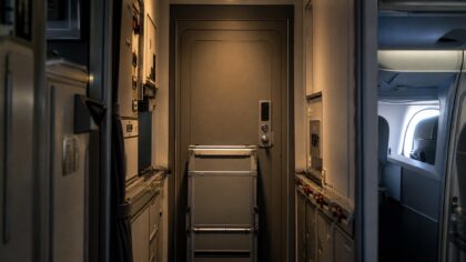 Locked reinforced flight deck door seen from the forward galley of an airliner, with a keypad lock and a galley cart parked across the aisle