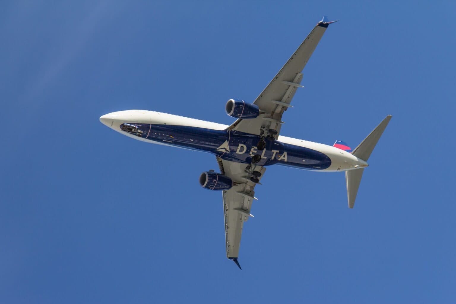 Delta Air Lines Boeing 737 seen from directly below, the DELTA wordmark across its dark blue belly against a clear blue sky