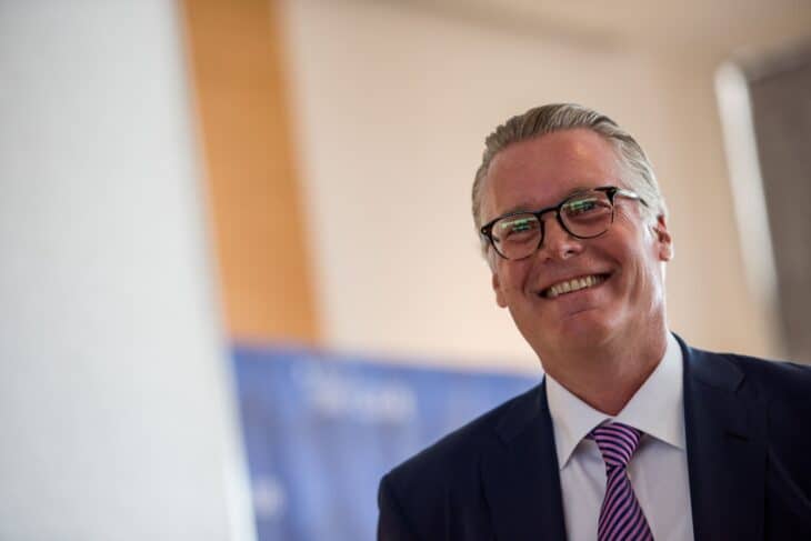 Delta Air Lines CEO Ed Bastian smiling in a dark suit and glasses at a Delta Sky Club opening