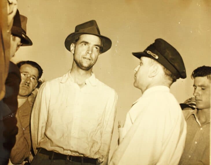 Howard Hughes in shirtsleeves and a hat, surrounded by crew and reporters during his 1938 round-the-world flight