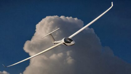 A white high-performance sailplane with very long slender wings banking against a dark blue sky and a sunlit cumulus cloud