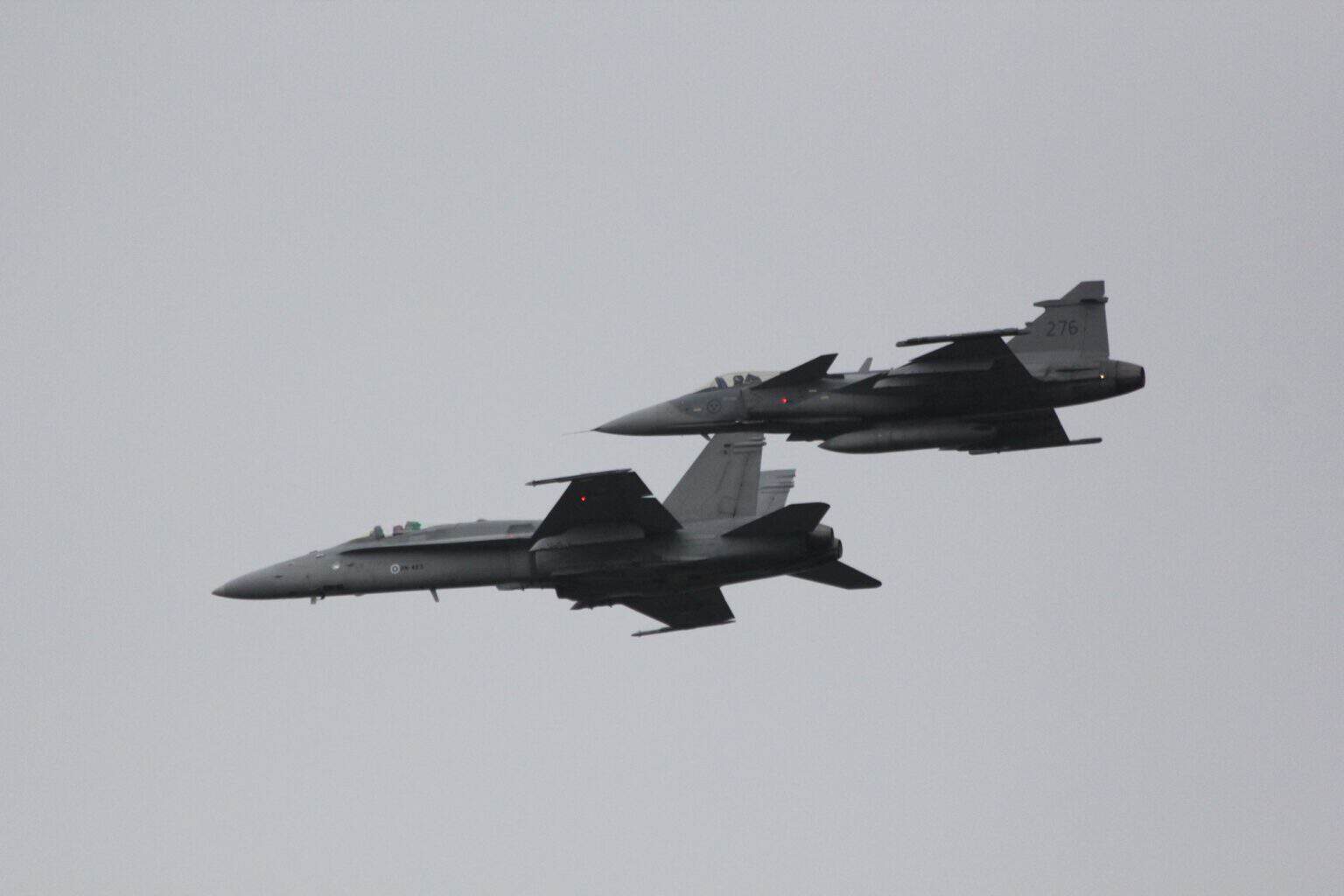 A gray Finnish Air Force F/A-18C Hornet and a Swedish Air Force JAS 39C Gripen, tail number 276, flying in close formation under an overcast sky