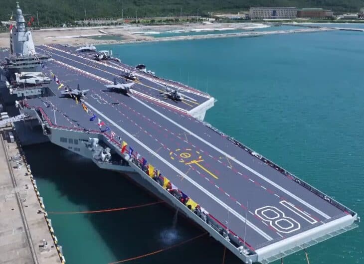 Aerial view of the Chinese aircraft carrier Fujian moored alongside a pier, its flat deck, catapult tracks and hull number 18 visible
