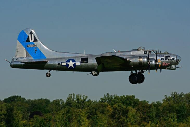 Boeing B-17G Sentimental Journey, N9323Z, in bare-metal finish with a blue tail band, flying low over trees with its landing gear down