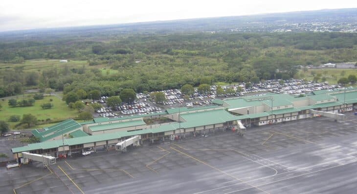 Aerial view of the Hilo International Airport terminal, its jet bridges and a wet apron, with forest and the town of Hilo beyond