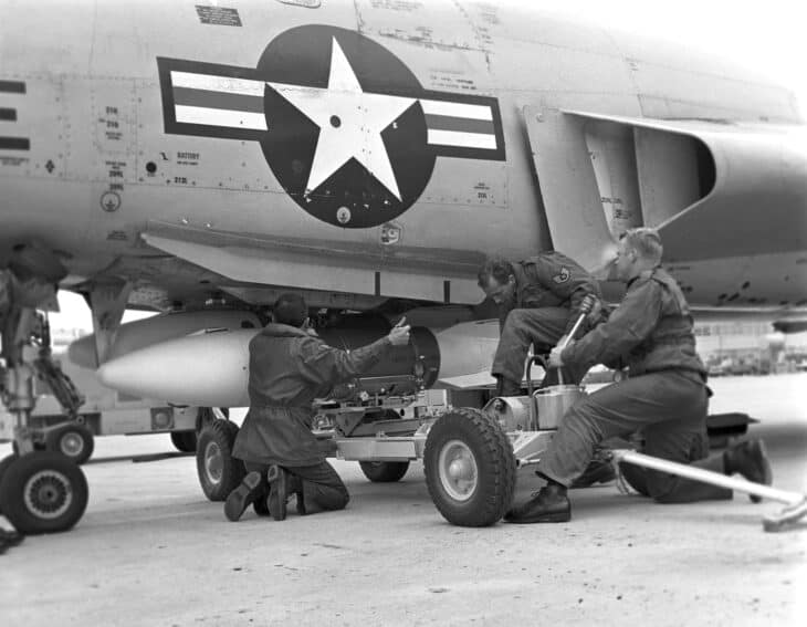 Two weapons handlers loading a training AIR-2 Genie rocket onto the belly of F-101B Voodoo 57-0252