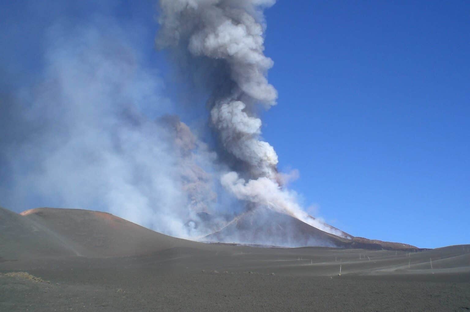 A column of volcanic ash rising from a summit crater of Mount Etna against a clear blue sky