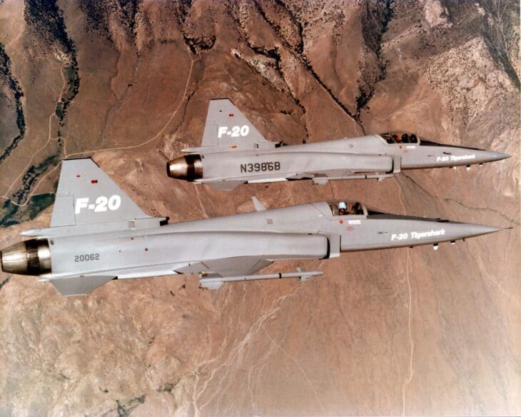 Two gray Northrop F-20 Tigershark prototypes, 82-0062 and N3986B, flying in formation over desert terrain
