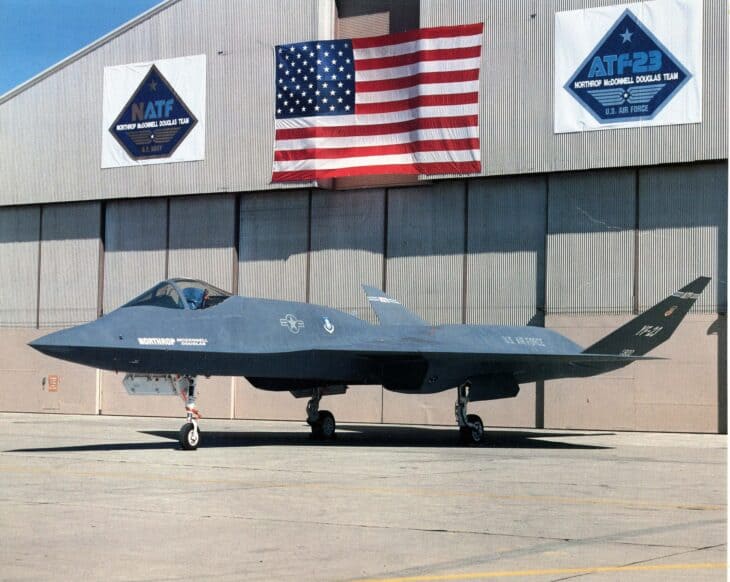 YF-23 PAV-1 parked in front of a hangar hung with an American flag and Northrop McDonnell Douglas ATF-23 and NATF banners