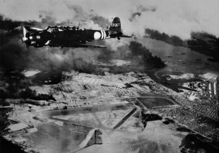 A Nakajima B5N2 Kate from the carrier Zuikaku, tail code EII-307, flying over Hickam Field as smoke rises from Pearl Harbor during the second wave