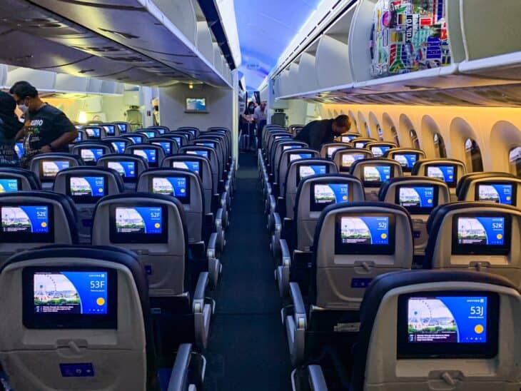 Economy cabin of a United Airlines Boeing 787-9 seen from the aisle, three seats on each side and three in the middle, seatback screens lit