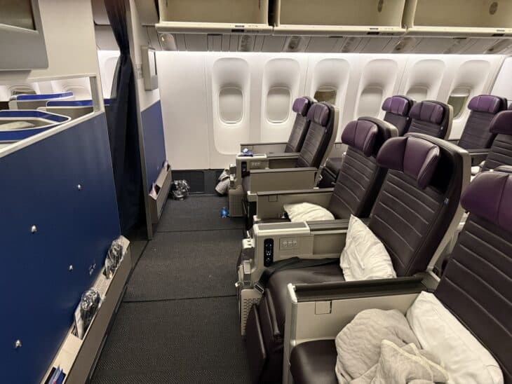 Front row of the United Premium Plus cabin on a Boeing 777-300ER, dark leather seats with pillows and blankets and a bulkhead leg area