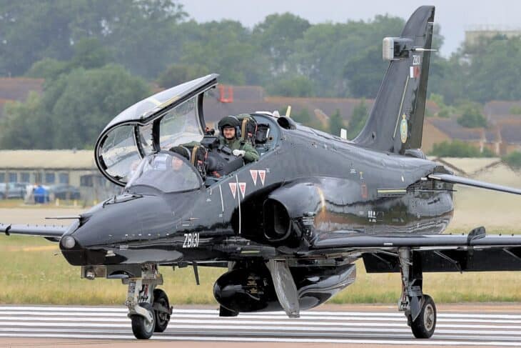A black RAF Hawk T2 taxiing with its canopy raised and two crew members in the tandem cockpit