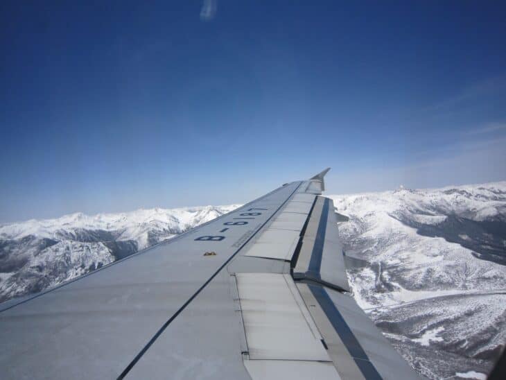 Airliner wing and extended trailing-edge flaps seen from a window seat behind the wing over snowy mountains
