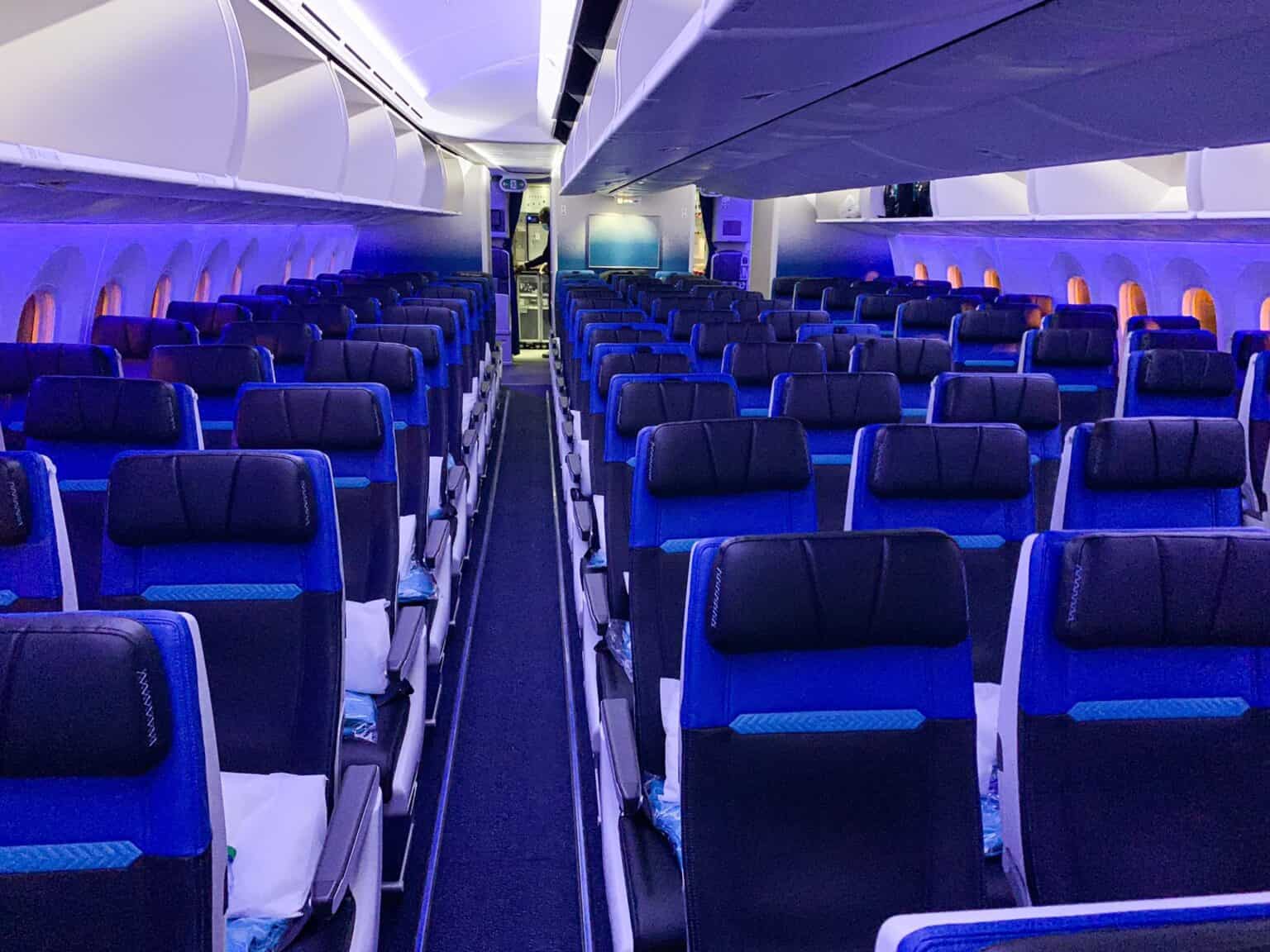 Rows of empty blue economy seats receding down the aisles of a WestJet Boeing 787-9 cabin under mood lighting