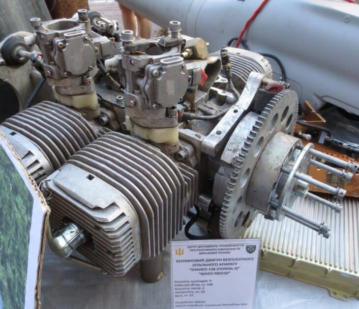 The four air-cooled cylinders and carburetor of a Shahed-136 MD550 piston engine on a display stand with a Ukrainian information placard