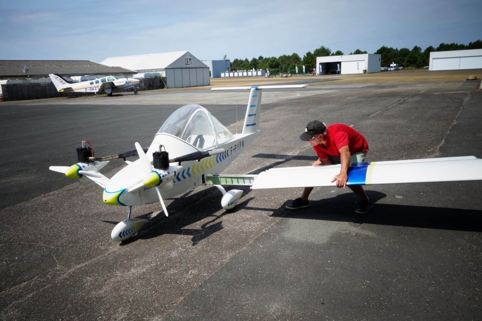 Man in a red shirt removing the detachable wing from a white Colomban Cri-Cri, F-PYPN, on an airfield ramp