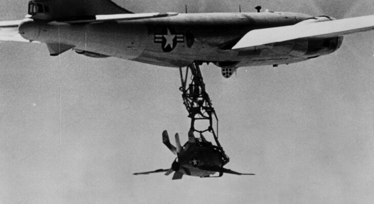 Black-and-white photo of the XF-85 Goblin hanging from the trapeze under its EB-29 mothership in flight