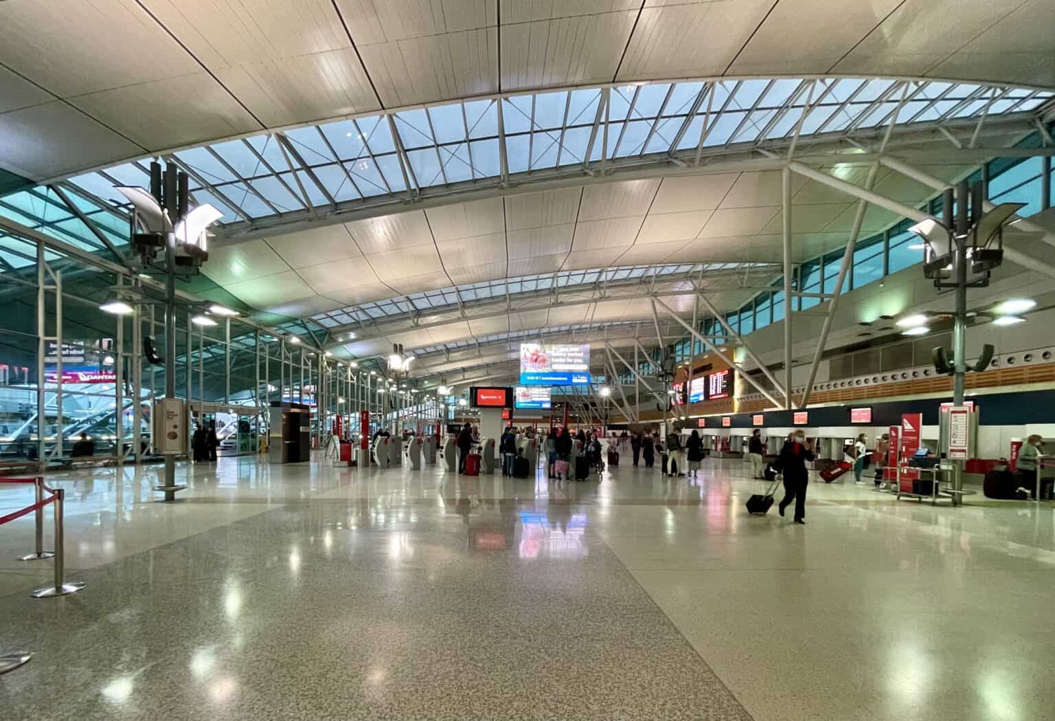 Passengers with luggage walking through the check-in hall of Sydney Airport Terminal 3 under its curved glass and steel roof