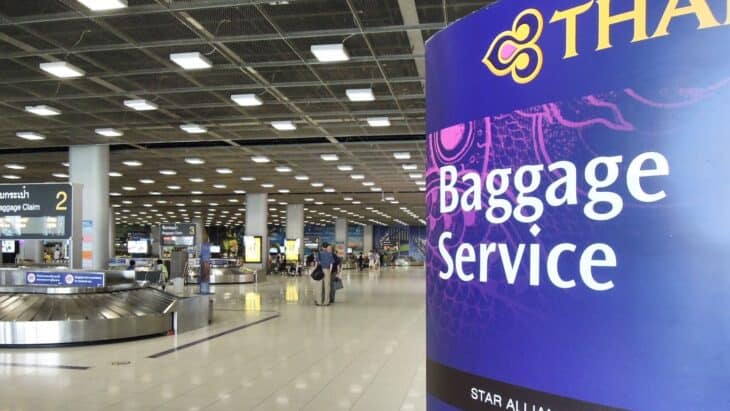 Baggage claim hall at Bangkok Suvarnabhumi Airport with a purple Thai Airways Baggage Service sign in the foreground