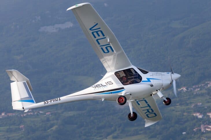 White Pipistrel Velis Electro two-seat electric trainer in flight over green countryside