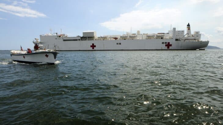 The hospital ship USNS Comfort, painted white with red crosses, seen from the water with a launch passing by