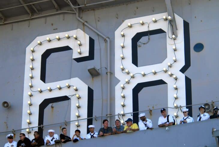 Sailors line the rails of the aircraft carrier USS Nimitz beside the ship's large painted hull number 68