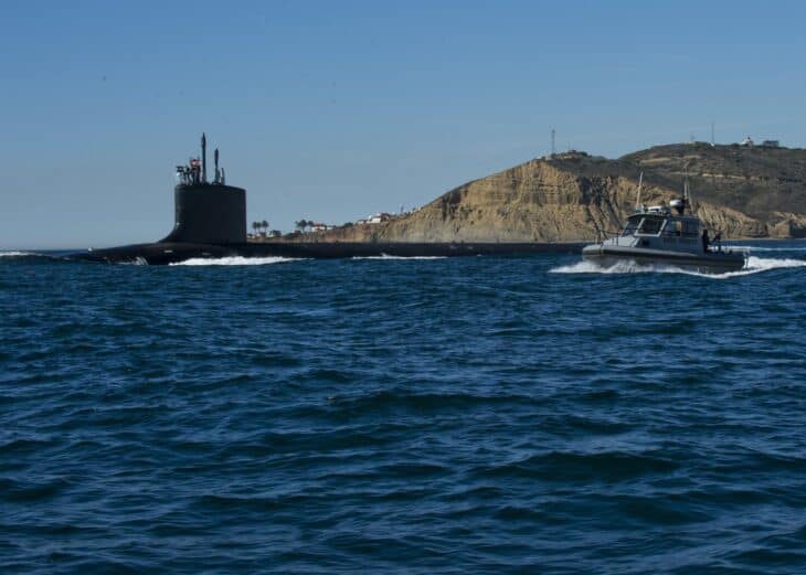 A Virginia-class fast attack submarine on the surface leaving San Diego harbour with an escort boat alongside