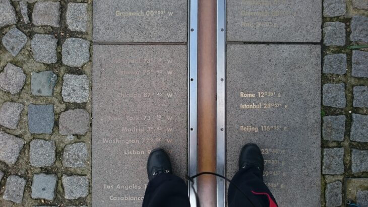A visitor standing astride the brass prime meridian line set into the cobbles at the Royal Observatory, Greenwich