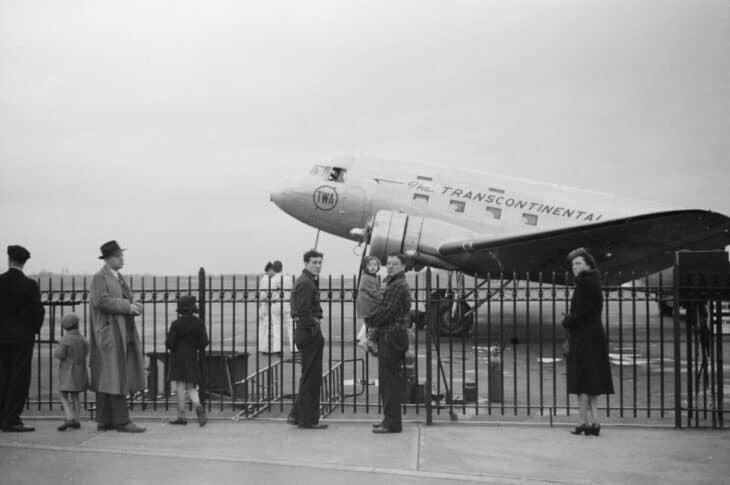 Black-and-white photograph of a Transcontinental and Western Air Douglas DC-3 on the ramp at an airport, with onlookers behind a fence