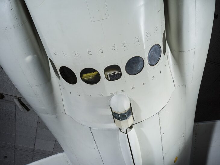 Underside of a white Lockheed U-2C fuselage showing a row of round camera windows in the equipment-bay hatch and a faceted glass driftsight housing below it.