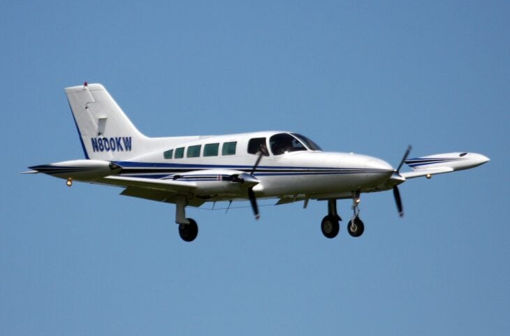 Cessna 402 twin-engine commuter with landing gear down on approach against a blue sky
