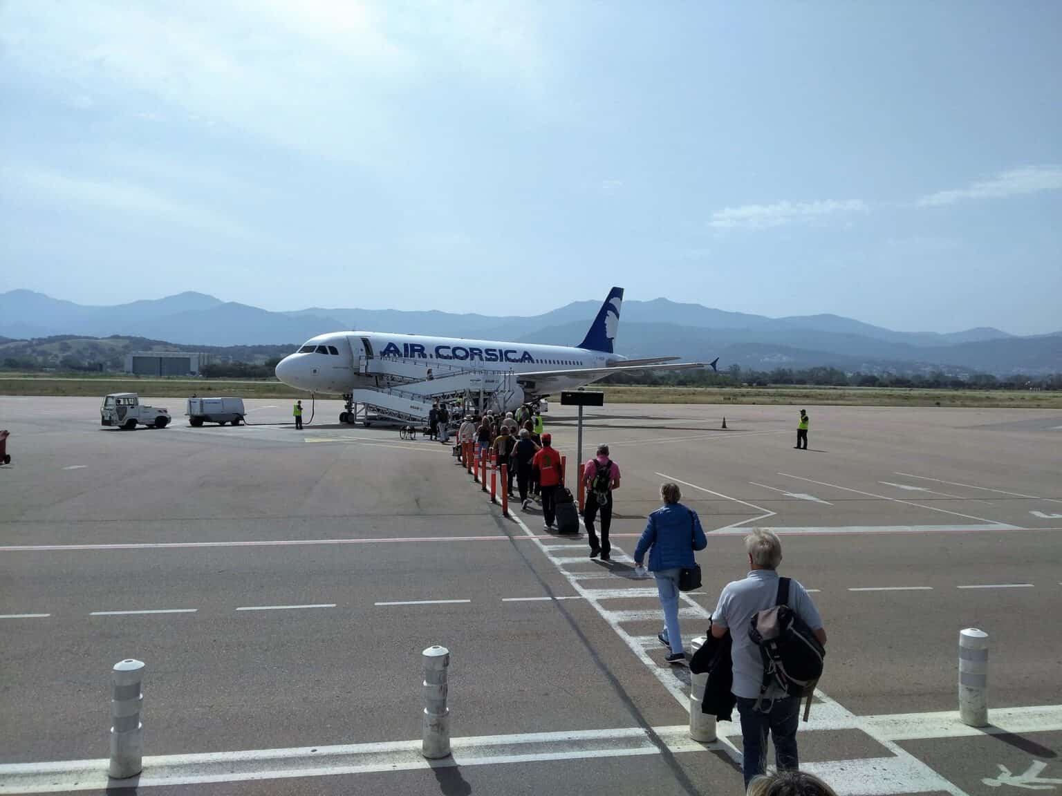 Passengers walking across the apron at Ajaccio Airport to board an Air Corsica Airbus A320, with Corsica's mountains behind