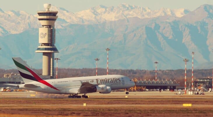 Control tower at Milan Malpensa with an Emirates Airbus A380 on the airfield and the Alps behind
