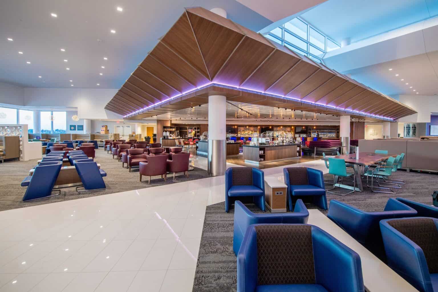 Wide view of a Delta Sky Club at Atlanta with an angled wooden ceiling, central bar and rows of blue lounge chairs