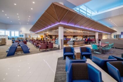 Wide view of a Delta Sky Club at Atlanta with an angled wooden ceiling, central bar and rows of blue lounge chairs
