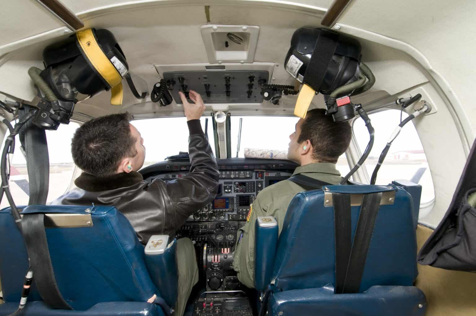 Two student pilots at the controls of a training aircraft cockpit with an instructor at the panel