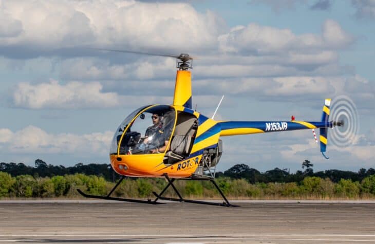 Yellow and blue Robinson R22 helicopter parked on a helipad