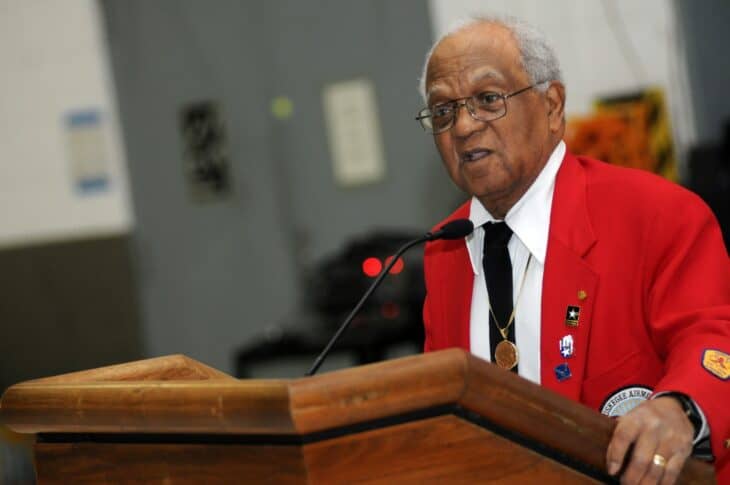 Tuskegee Airman speaking at a podium in a red jacket