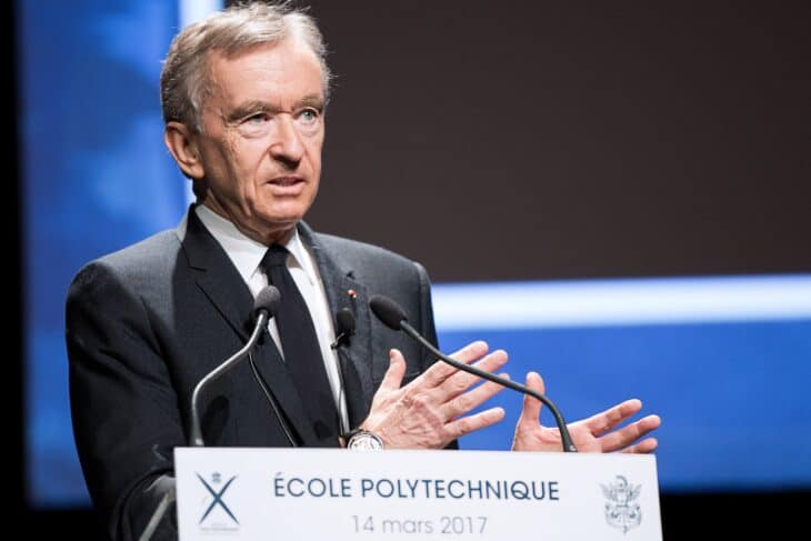Bernard Arnault speaking at a podium at a 2017 event, hands raised mid-sentence