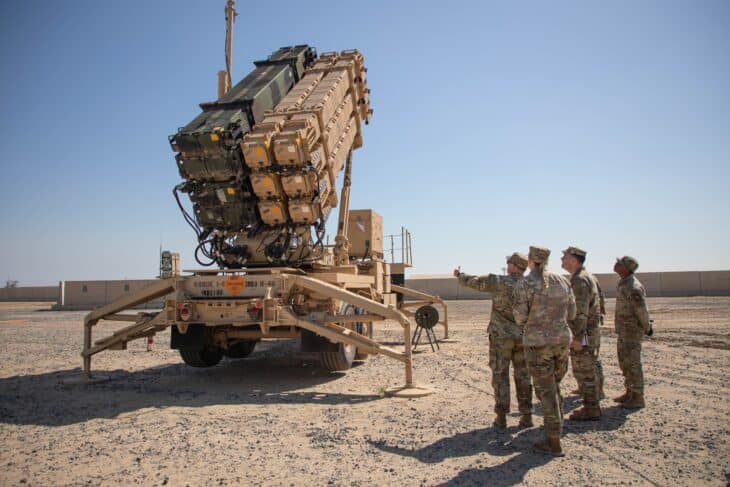 Soldiers standing beside a Patriot launcher with its missile canisters raised in desert terrain