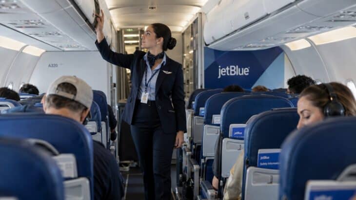 A JetBlue flight attendant checking an overhead bin while walking the aisle