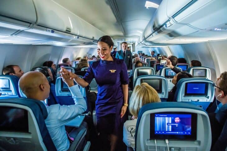Delta flight attendant in a purple uniform walking the cabin aisle during a mid-flight uniform showcase