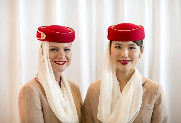 Two Emirates cabin crew in red hats and white veils smiling at the camera